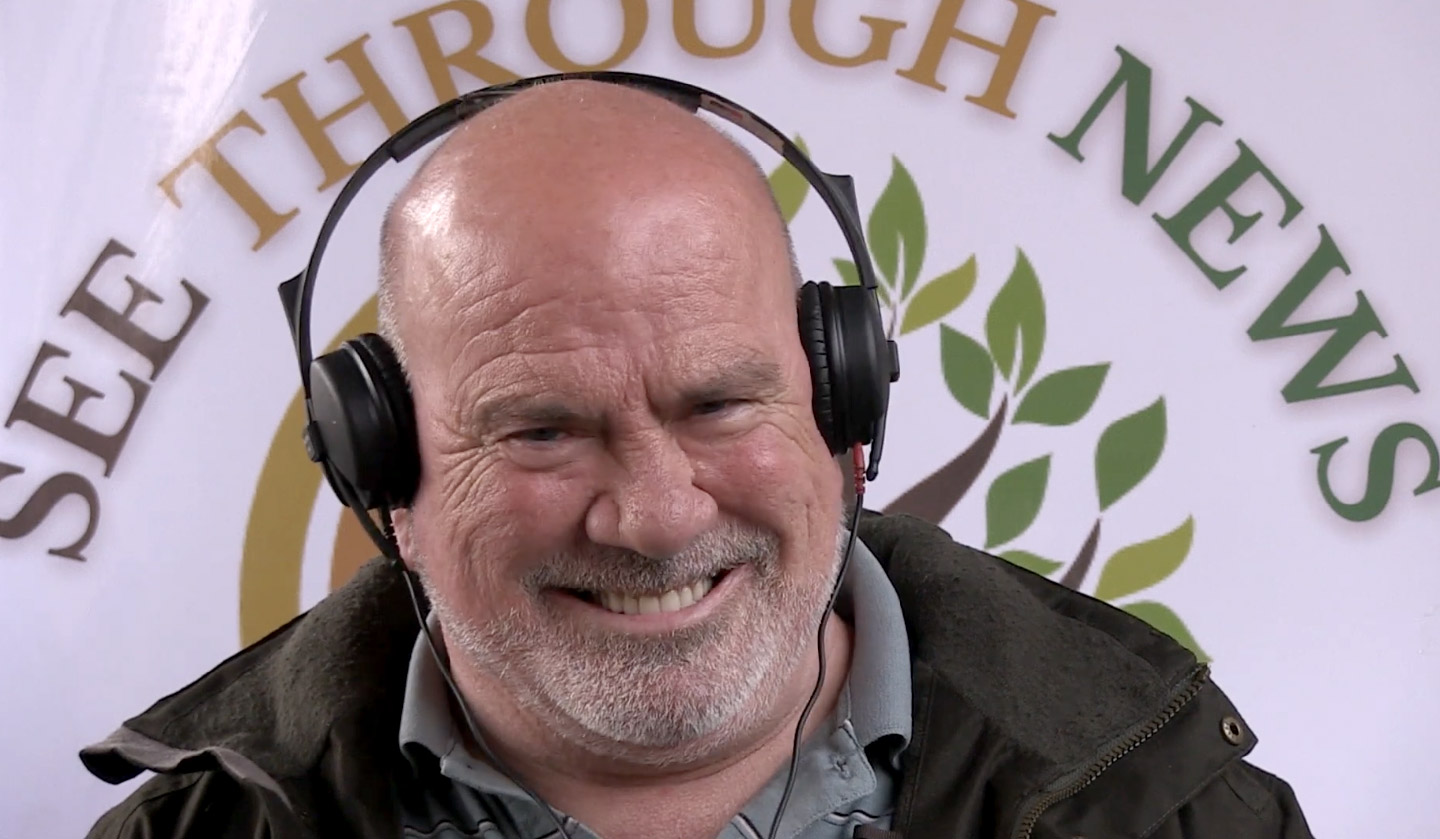 Watch Chris from Appleby play The Think Game. (Chris is smiling and wearing headphones while seated in front of a See Through News backdrop.)