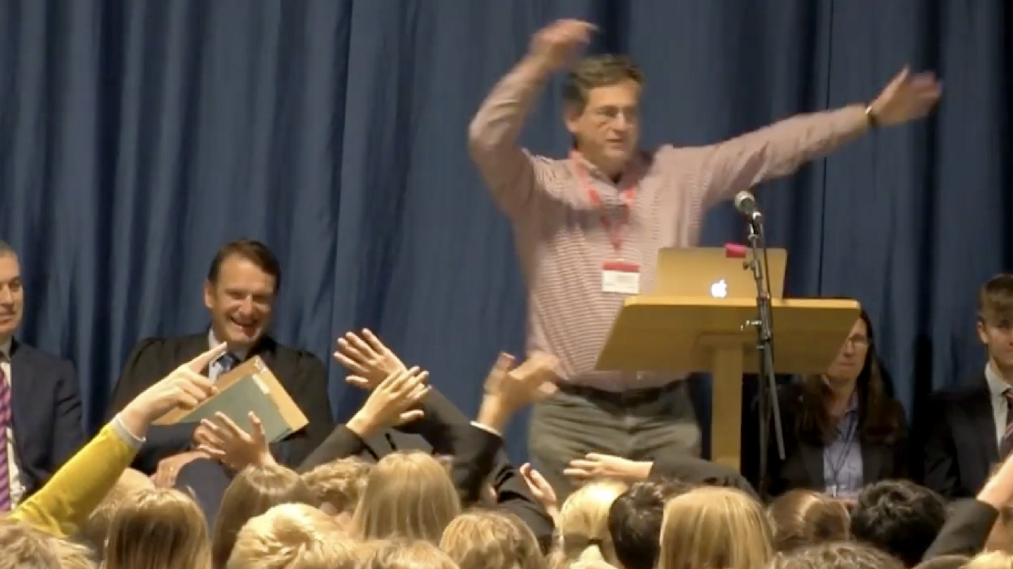 Watch ‘Speaking of… Climate and Language’. (Robert Stern stands, waving his arms at the students assembled in front of him. Alongside him on stage some of the teaching staff are laughing in enjoyment.)